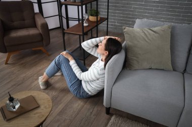 Evdeki kanepenin yanında oturan depresyondaki genç kadın.