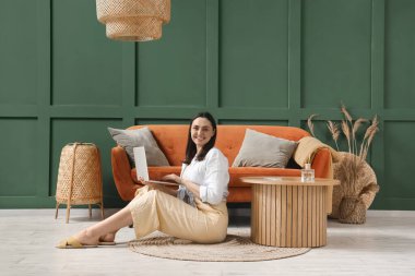 Evdeki kırmızı kanepenin yanında dizüstü bilgisayar kullanan genç bir kadın.