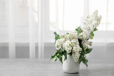 Odanın penceresinin yanındaki masada leylak dalları olan vazo.