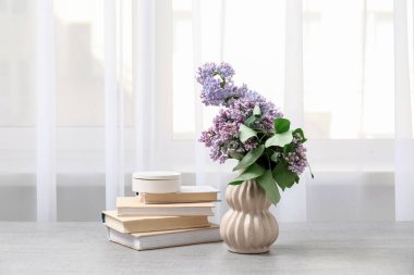 Odadaki pencerenin yanındaki masada leylak dallı kitap ve vazo.