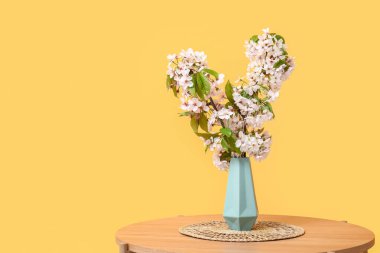 Turuncu duvarın yanındaki sehpanın üzerinde çiçek açan dalları olan vazo.