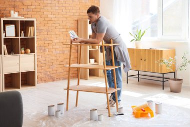 Evde boya rengi paletleri ve raf ünitesi olan genç bir adam var.