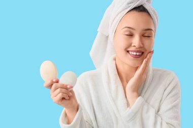 Bornozlu, mavi arka planda sabun barları olan genç Asyalı kadın, yakın plan.