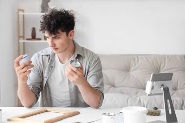 Konserve kutularıyla evde çerçeve boyayan genç adam.