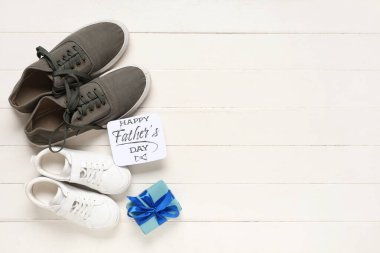 Erkek ve çocuk ayakkabıları, hediye kutusu ve beyaz tahta arka planda Mutlu Babalar Günü yazılı tebrik kartı. Üst görünüm