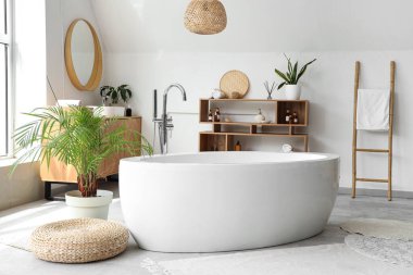 İçinde seramik küvet ve bitkiler olan hafif bir banyo.