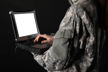 Askeri dizüstü bilgisayarı tutan üniformalı asker siyah arka planda boş ekranlı.