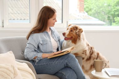 Evde sevimli bir Avustralya çoban köpeği olan genç bir kadın kitap okuyor.