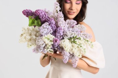 Açık arkaplanda leylak çiçekleri olan güzel bir genç kadın, yakın plan.