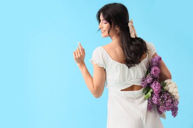 Mavi arka planda, çantasında leylak çiçekleri olan güzel genç bir kadın.