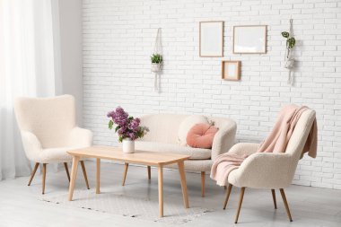 Oturma odasında, sehpanın üzerinde bir buket leylak dalı, beyaz koltuklar ve kanepe var.