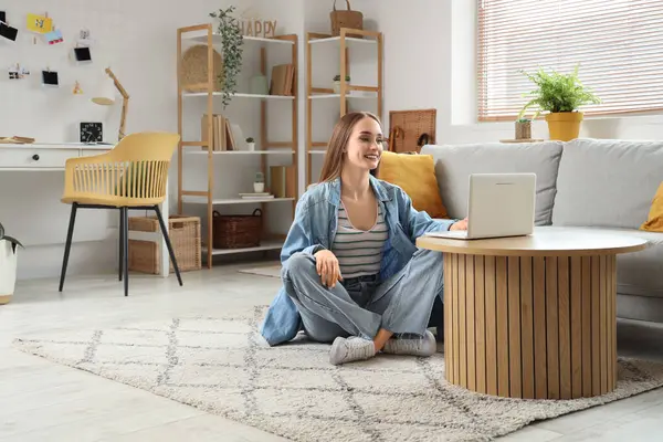 Genç ve güzel bir kadın oturma odasında dizüstü bilgisayar kullanıyor.