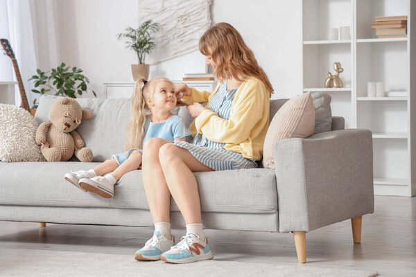 Няня расчесывает девочке волосы на диване дома