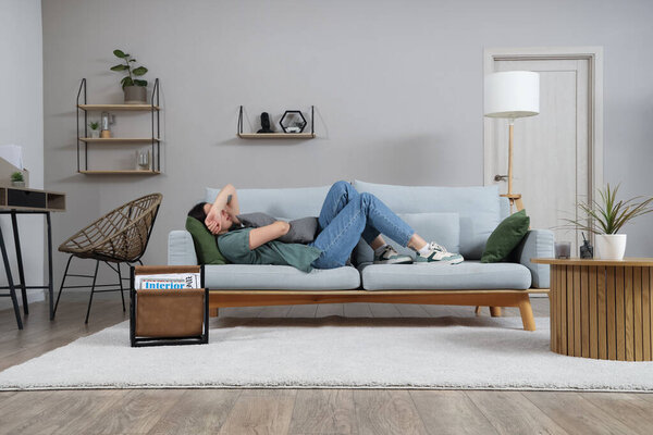 Depressed young woman with pillow lying on sofa at home