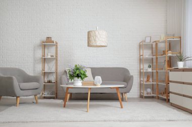 Güzel bir çiçek buketi, kitaplar, masa üzerinde lamba, kanepe ve oturma odasının içinde raf ünitesi olan beyaz vazo.