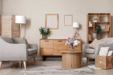 Koltuk, çekmece, masa ve çiçekler şık bir oturma odasında.