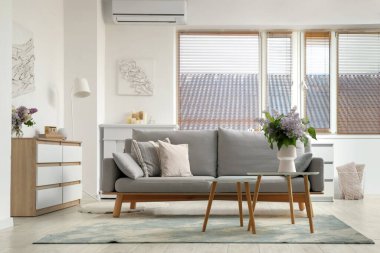 Vazoda çiçekli masa ve şık oturma odasının iç tarafındaki pencerenin yanındaki gri kanepe.