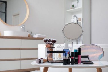 Dekoratif kozmetik ürünleri, ayna ve fırçalar olan masa.