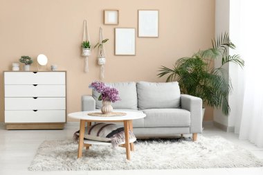 Gri kanepenin yanındaki sehpanın üzerinde bir demet leylak dalı olan oturma odasının içinde.