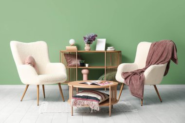 Beyaz koltukların yanındaki sehpanın üzerinde bir demet leylak dalı olan oturma odasının içinde.