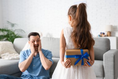 Küçük kız, babasını oturma odasında şaşırtıyor. Babalar günü kutlaması.