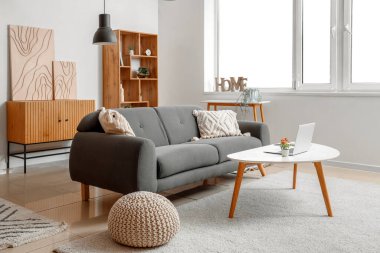 Aydınlık oturma odasının içinde siyah kanepe, raf ünitesi, sehpa ve modern dizüstü bilgisayar var.