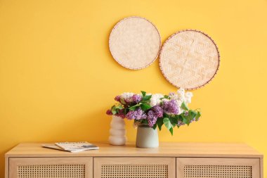 Sarı duvarın yanındaki dolapta çiçekli vazo var.