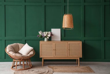 Oturma odasındaki yeşil duvarın yanındaki yastıklı ve ahşap dolaplı koltuk.