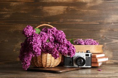 Tahta arka planda çiçek açan leylak çiçekleri, kitaplar ve fotoğraf makinesi olan sepet.