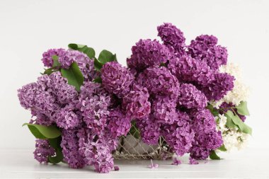 Beyaz ahşap masada çiçek açan leylak rengi sepet.