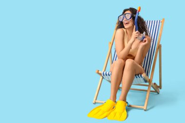 Mavi arka planda güverte koltuğunda oturan gözlüklü ve paletli güzel Afro-Amerikalı kadın.