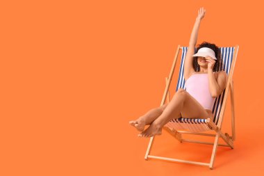 Şapkalı güzel Afro-Amerikalı kadın turuncu arka planda, iskemlede oturuyor.