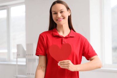 Klinikte uygulamalı yaması ve kağıt kalbi olan bir kadın kan bağışçısı.