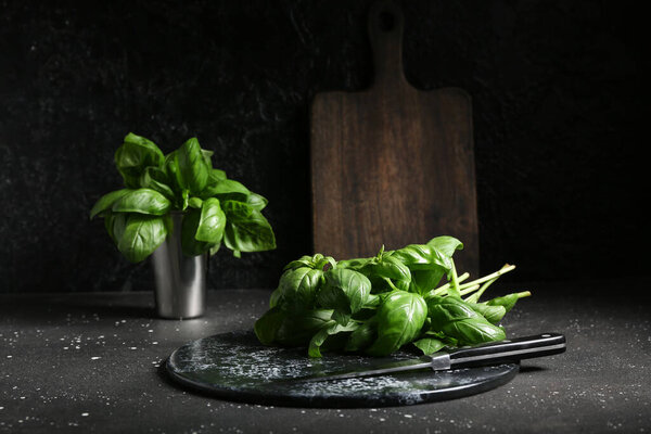 Board with fresh green basil leaves on black background