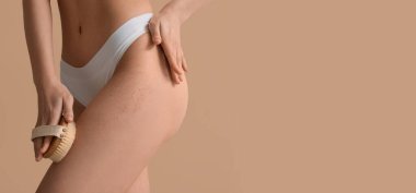 Bej arka planda masaj fırçasıyla vücudunu fırçalayan genç bir kadın. Mesaj için yeri var, yakın plan.