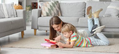 Küçük çocuk ve annesi evde yerde yatarken kitap okuyorlar.