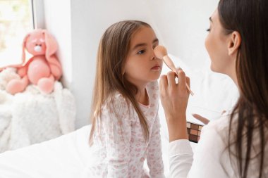 Mutlu anne ve küçük kızı yatak odasında makyaj yapıyor, yakın çekim.