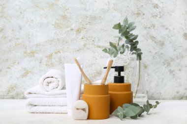 Masanın üzerinde okaliptüs dalları ve grunge arka planında farklı banyo malzemeleri var.