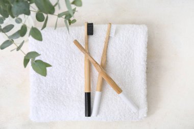Bambu diş fırçaları, temiz havlu ve arka planda okaliptüs dalları.