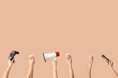 Patlamış mısırlı kovaları tutan eller, oyun yastığı, üç boyutlu gözlükler ve bej arka planda megafon.