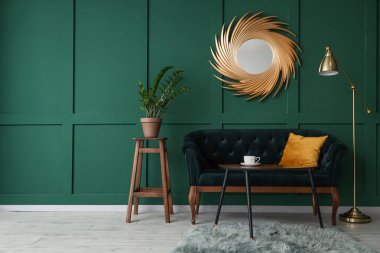 Yeşil duvarın yanında ayna ve lamba olan rahat bir kanepe.