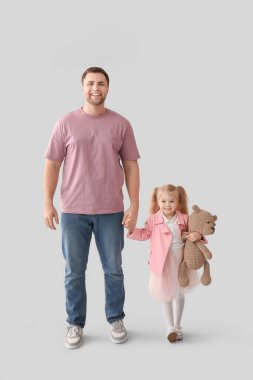 Mutlu babası ve tatlı küçük kızı gri arka planda oyuncak ayısıyla