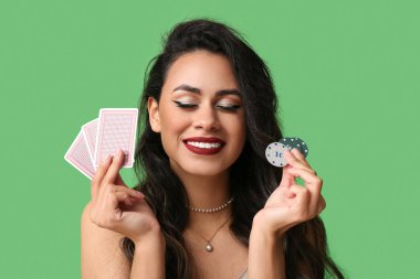 Yeşil arka planda oyun kartları ve poker fişleri olan güzel bir Afro-Amerikalı kadın.