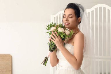 Düğün buketi olan genç gelin, arka planda katlanan perdenin yanında.