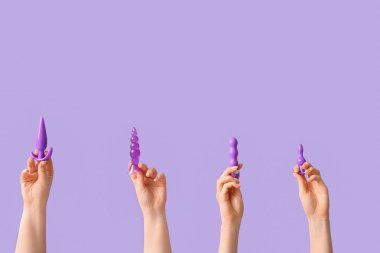 Leylak arka planında anal tıkaçları ve vibratörü olan kadın elleri.