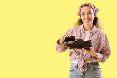 Kadın ayakkabıcı, sarı arka planda çizme parlatıyor.