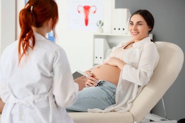 Kanepede genç hamile bir kadın klinikteki doktoru ziyaret ediyor.