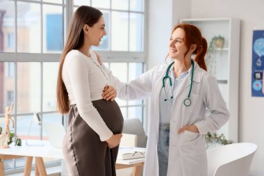 Kadın doktor klinikte hamile bir kadınla konuşuyor.
