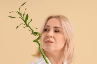 Bej arka planda bambu dalı olan güzel olgun, mutlu bir kadın.