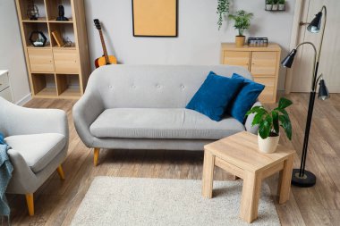 Interior of light living room with grey sofa, table and armchair